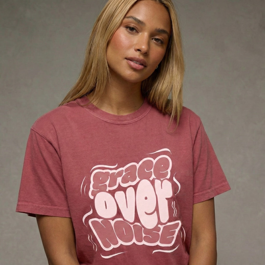 Woman wearing a maroon Grace Over Noise unisex t-shirt with white bubbly streetwear typography by Way Is Made
