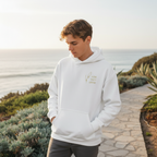 Person wearing a white hoodie with text, standing on a path near the ocean.