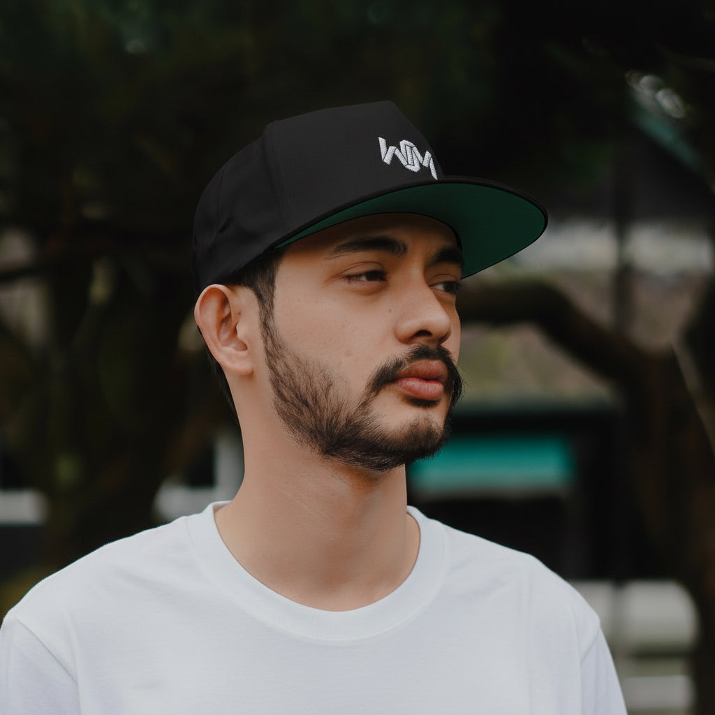 Man wearing a black cap with a logo, looking to the side with a blurred outdoor background