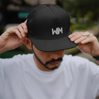 Person wearing a black cap with a logo, against a blurred natural background