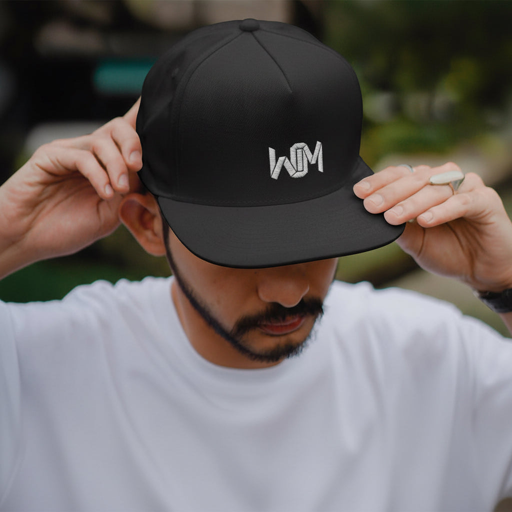 Person wearing a black cap with a logo, against a blurred natural background